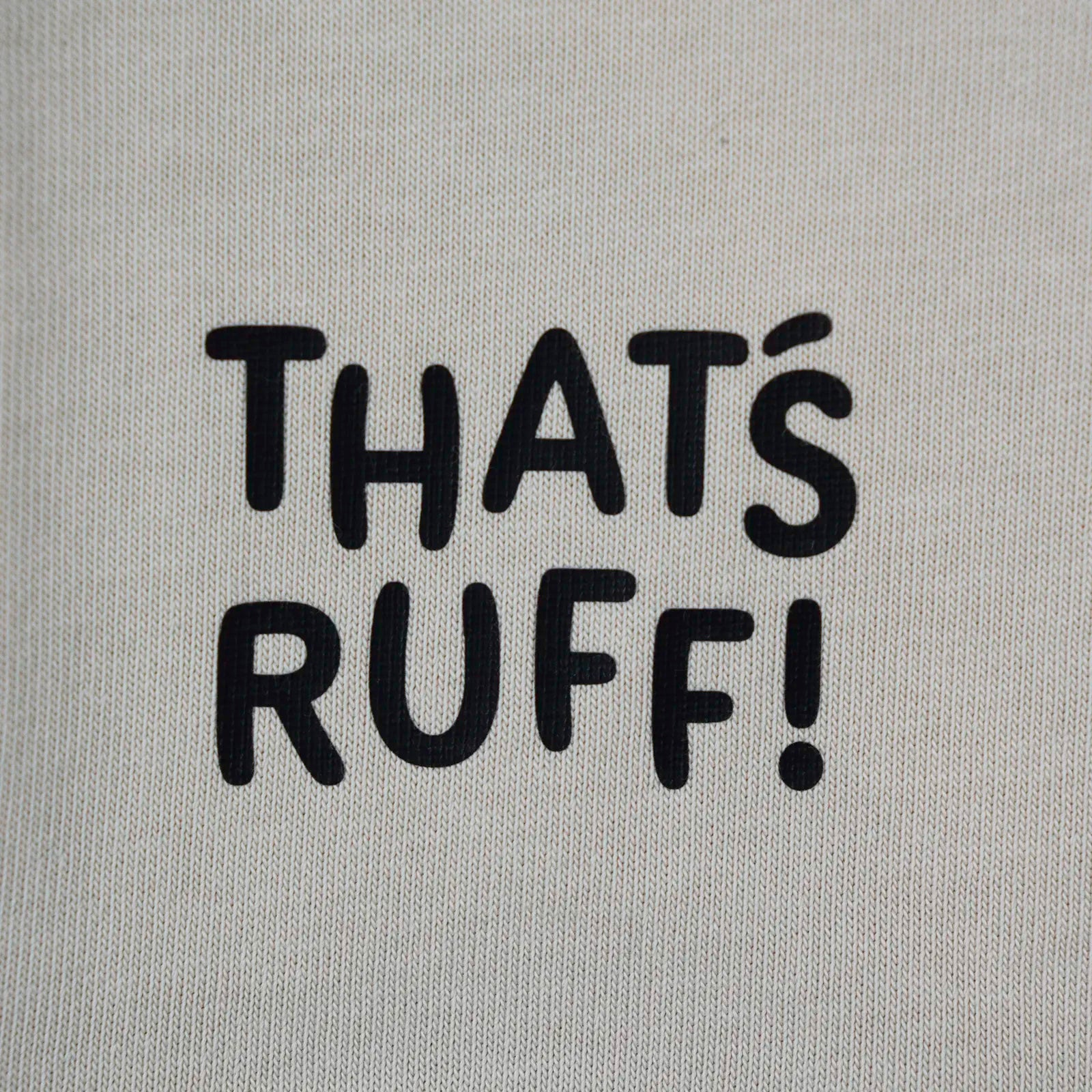 Detail of the THAT'S RUFF hem print on a beige tee—simple branding on a premium cotton basic.