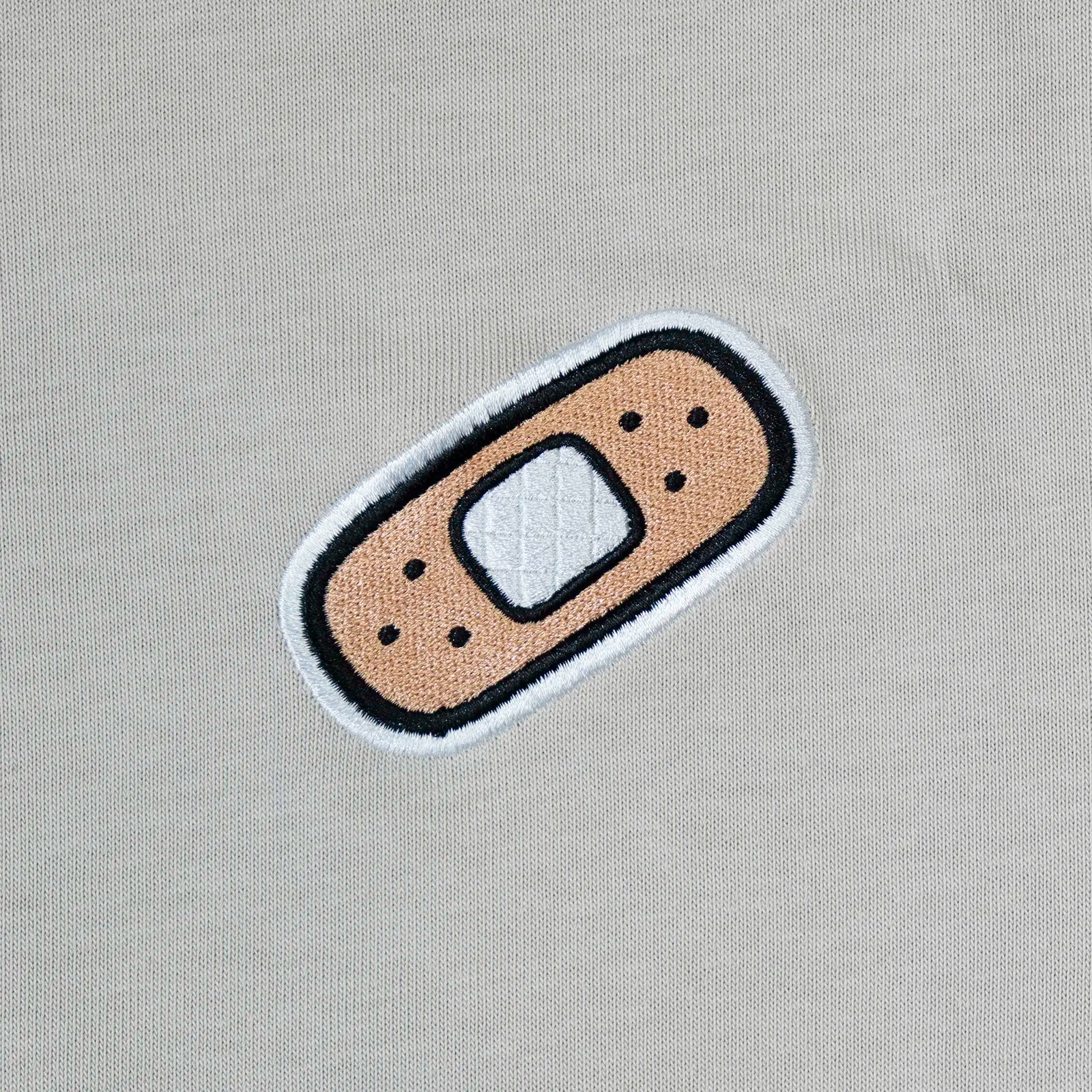 Small plaster patch chest embroidery on beige t-shirt—cute, low-key graphic for kawaii outfits.