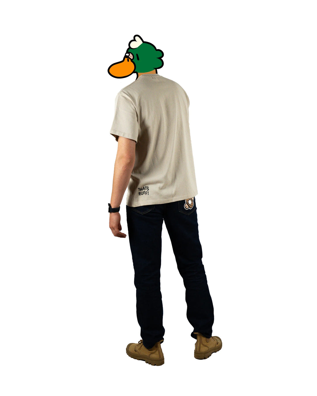 Full-body view of a model wearing a beige t-shirt with a bandage graphic on the chest and patched black pants featuring 'That's Ruff!' designs. Paired with sneakers, this outfit showcases a bold and casual look from the 'That's Ruff!' collection.