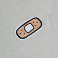 Small plaster patch chest embroidery on beige t-shirt—cute, low-key graphic for kawaii outfits.