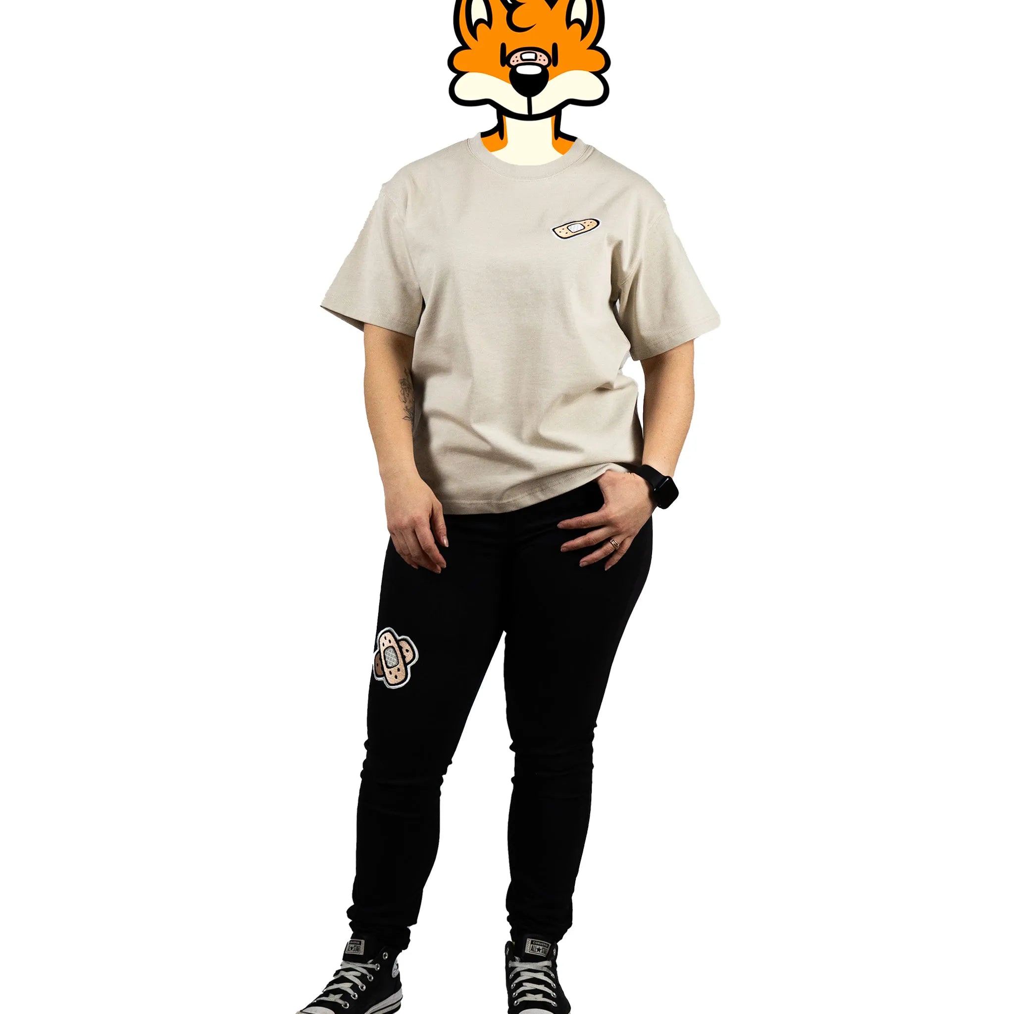 Full-body view of a model wearing a beige t-shirt with a bandage graphic on the chest and patched black pants featuring 'That's Ruff!' designs. Paired with sneakers, this outfit showcases a bold and casual look from the 'That's Ruff!' collection.