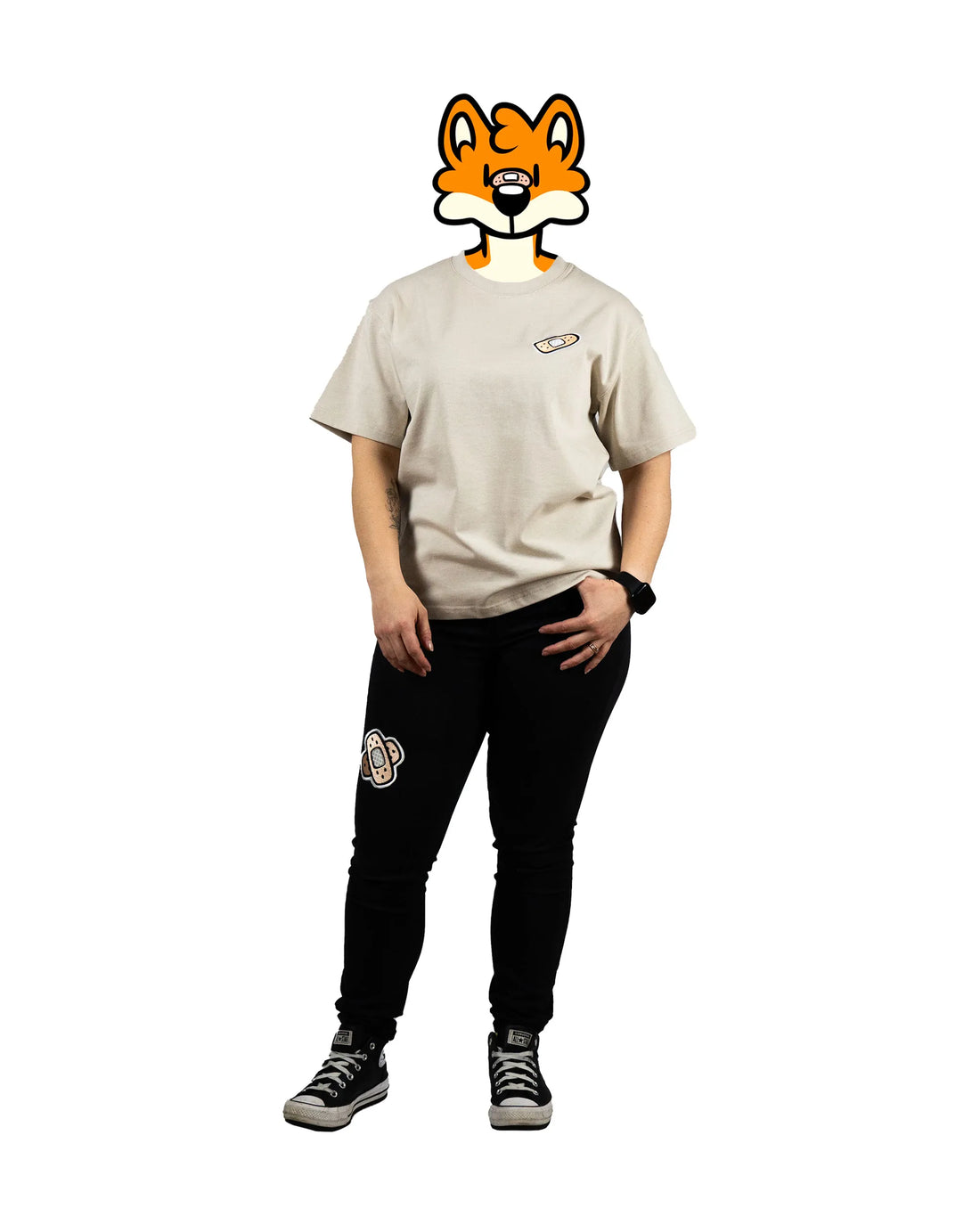 Full-body view of a model wearing a beige t-shirt with a bandage graphic on the chest and patched black pants featuring 'That's Ruff!' designs. Paired with sneakers, this outfit showcases a bold and casual look from the 'That's Ruff!' collection.
