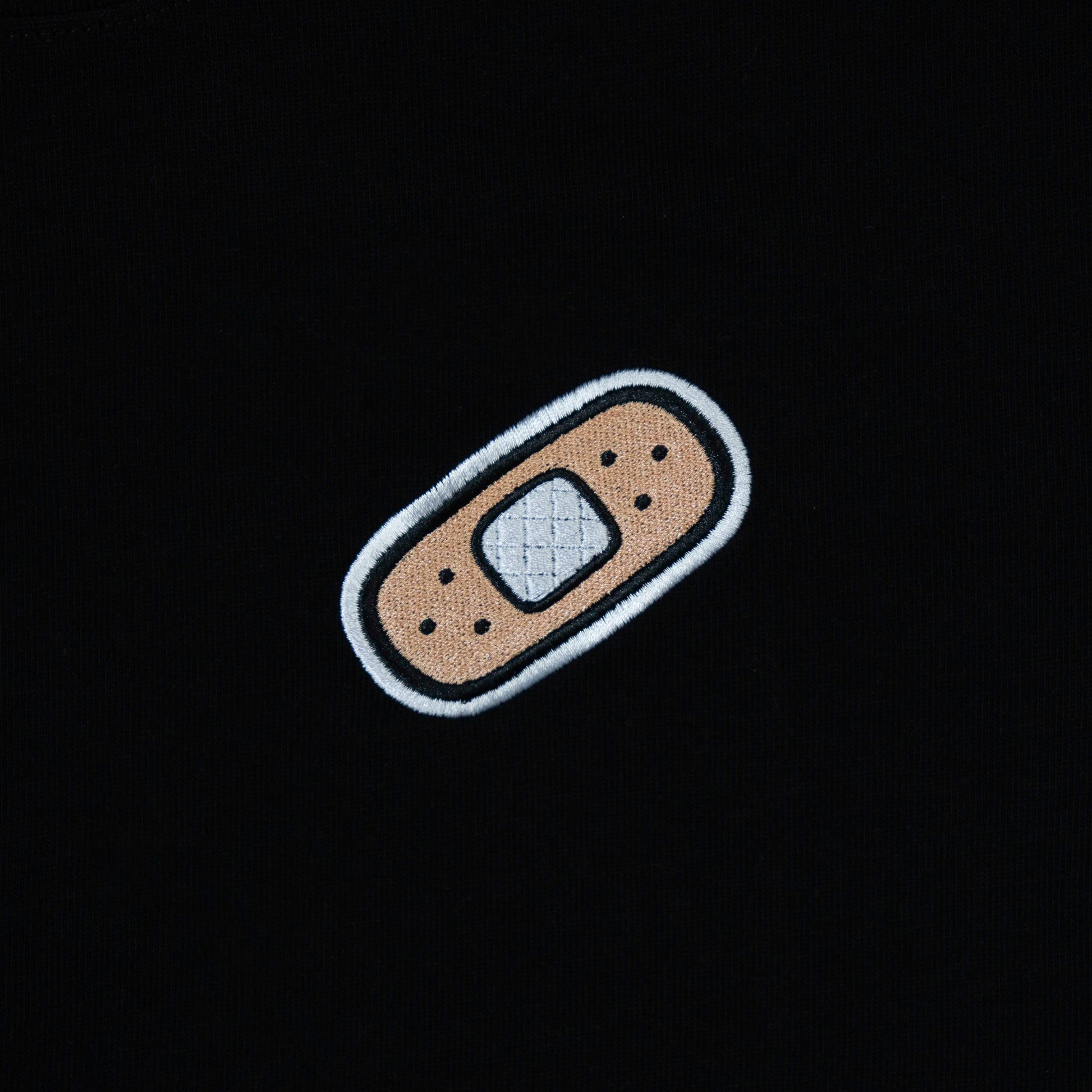 Bandage patch chest embroidery on black t-shirt—minimal graphic for casual and kawaii streetwear looks.