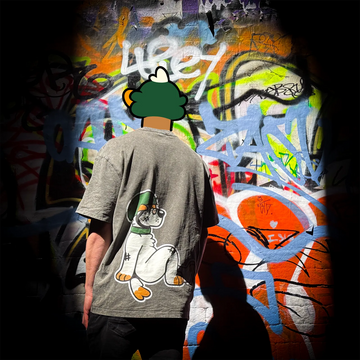 Person wearing a gray t-shirt with a cartoon character on the back, standing in front of a colorful graffiti wall.