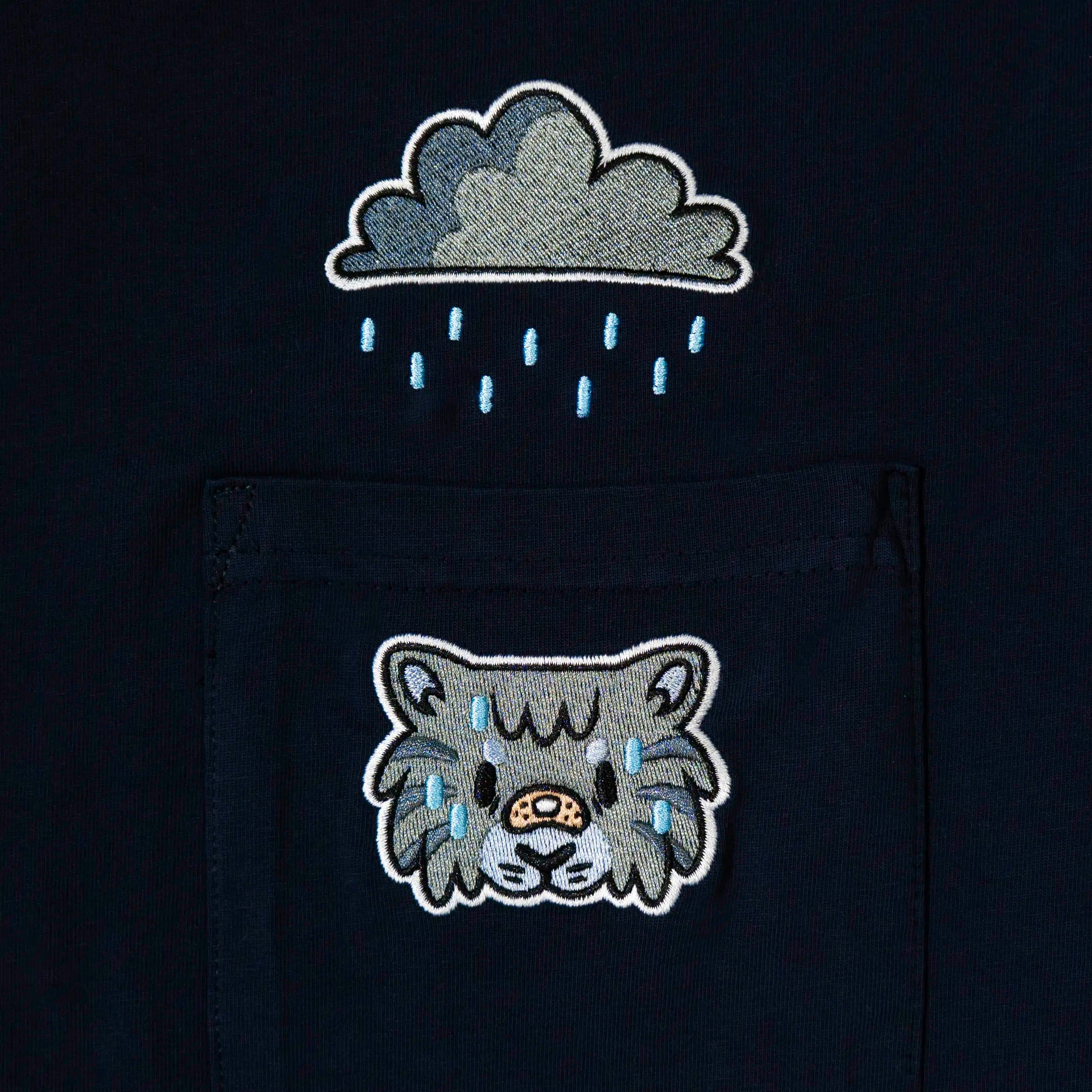 Close-up of embroidered tabby cat in rain above the pocket on dark navy tee—cute animal design for furry clothing.