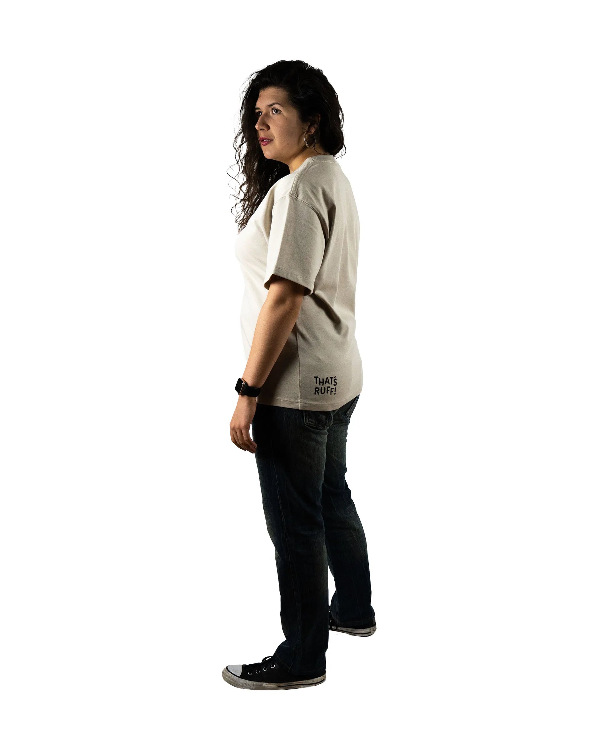 Side view of a model wearing a beige t-shirt with the 'That's Ruff!' logo near the hem. Paired with jeans and sneakers, this casual outfit emphasizes versatile and stylish fashion from the 'That's Ruff!' collection.