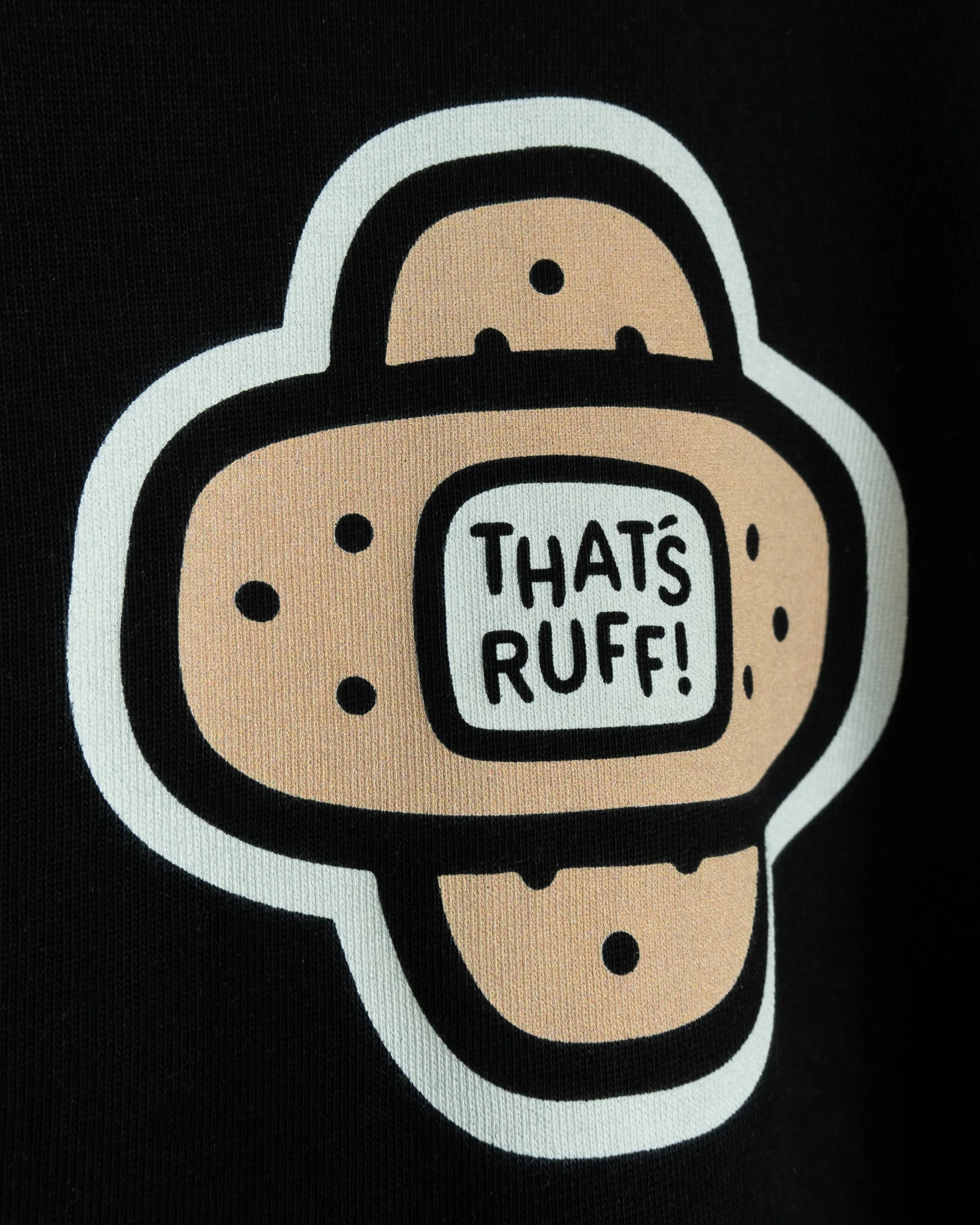 Close-up view of the bold 'That's Ruff!' bandage logo printed on a black t-shirt. This vibrant, playful design showcases the brand's fun and edgy aesthetic.
