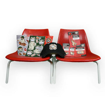 Merchandise display from the 'That's Ruff!' collection featuring sticker sheets, enamel pins, and a black cap with a bandage graphic. Arranged on two vibrant red chairs, this showcase highlights bold cartoon designs perfect for fans of playful and creative streetwear-inspired accessories.
